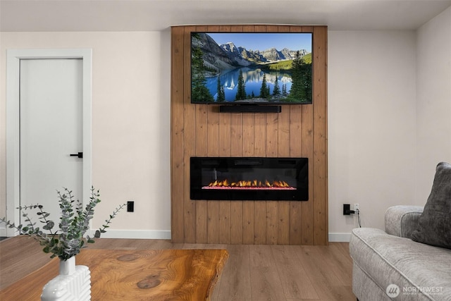 living room featuring wood finished floors, a glass covered fireplace, and baseboards