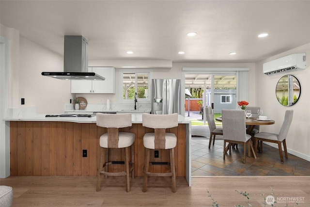kitchen with island exhaust hood, an AC wall unit, a sink, recessed lighting, and a peninsula