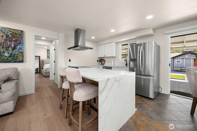 kitchen with stainless steel fridge, extractor fan, stovetop, light stone countertops, and a breakfast bar area