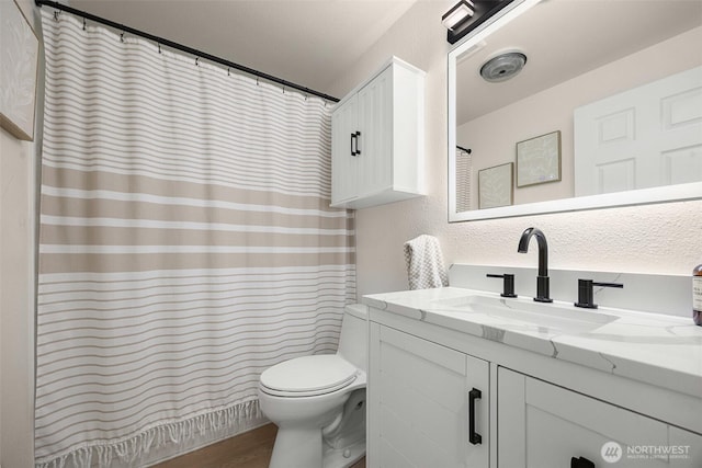 bathroom with toilet, wood finished floors, vanity, curtained shower, and a textured wall