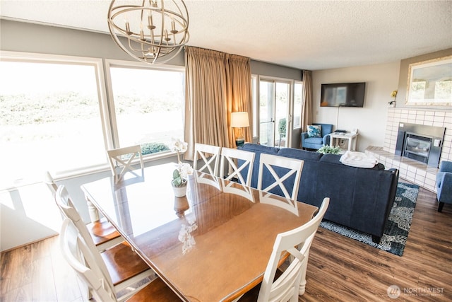 dining space with an inviting chandelier, a textured ceiling, a glass covered fireplace, and wood finished floors