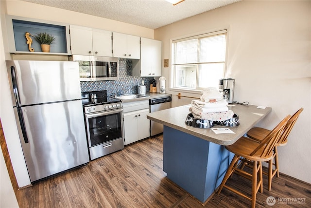 kitchen featuring a peninsula, dark wood-type flooring, white cabinetry, backsplash, and appliances with stainless steel finishes