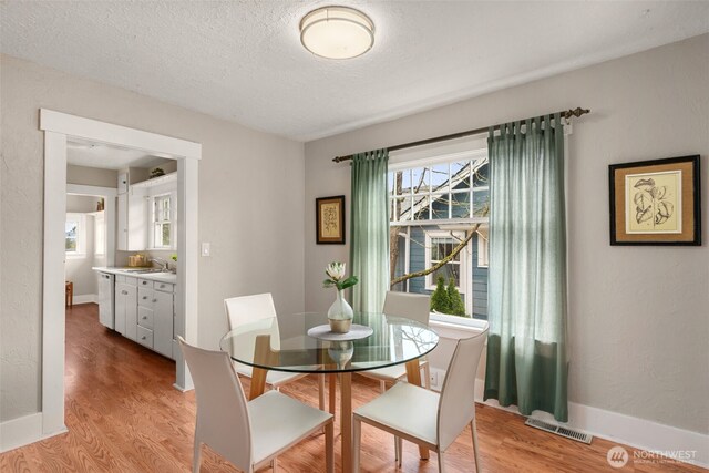 dining area with light wood-style floors, a textured ceiling, and baseboards
