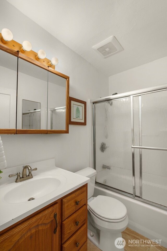 bathroom featuring vanity, combined bath / shower with glass door, and toilet