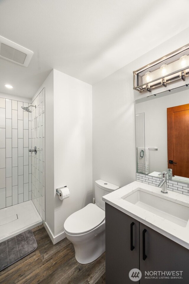 full bathroom with toilet, a tile shower, wood finished floors, vanity, and baseboards