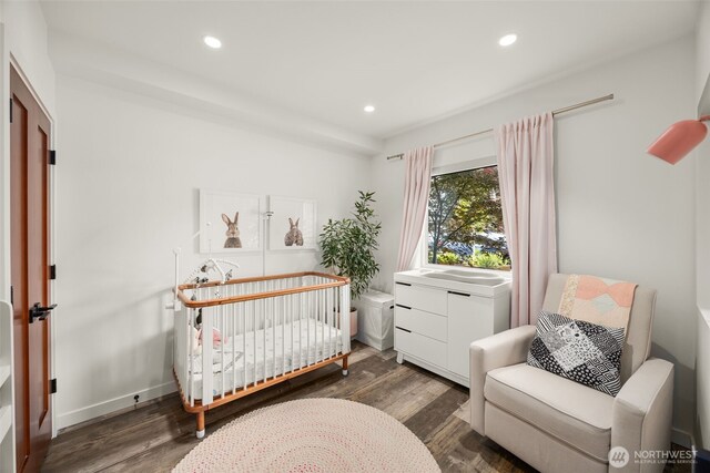 bedroom with wood finished floors, recessed lighting, a crib, and baseboards