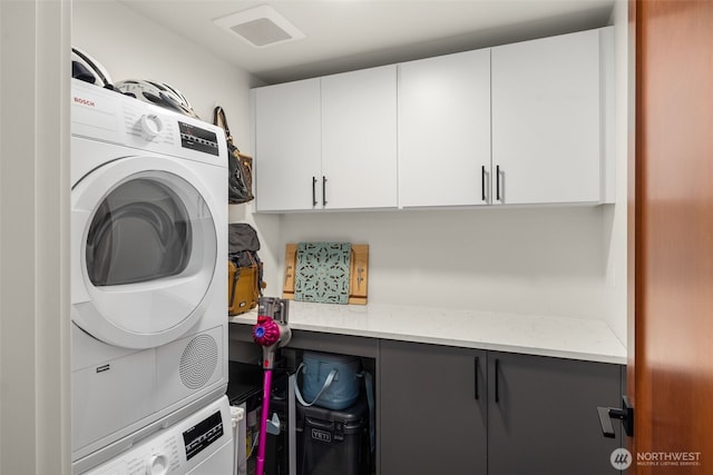 clothes washing area with stacked washer / dryer and cabinet space