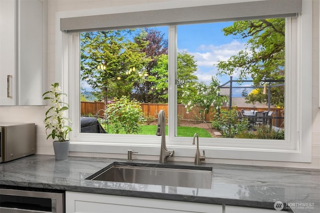 kitchen view of a sink, white cabinetry, dark stone countertops, and beverage cooler