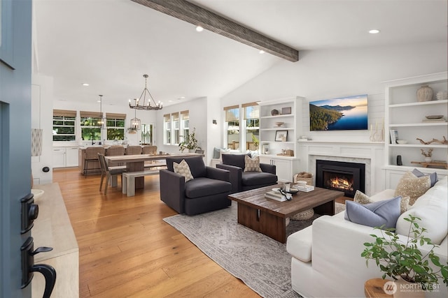 living room featuring a warm lit fireplace, a chandelier, light wood-type flooring, and recessed lighting