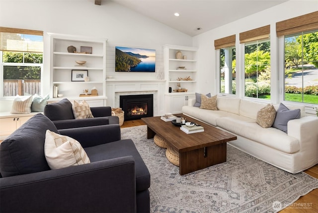 living area featuring healthy amount of natural light, wood finished floors, lofted ceiling, a warm lit fireplace, and recessed lighting