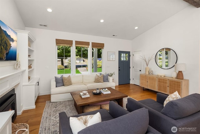 living room featuring light wood-type flooring, a glass covered fireplace, healthy amount of natural light, lofted ceiling, and recessed lighting