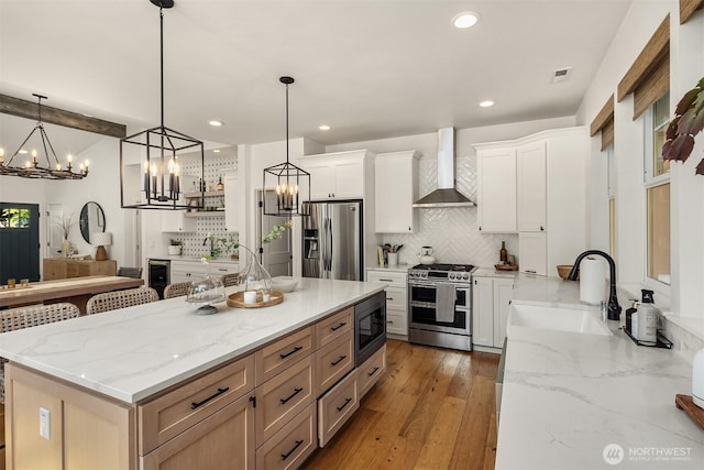 kitchen with stainless steel appliances, a sink, wall chimney range hood, a chandelier, and backsplash