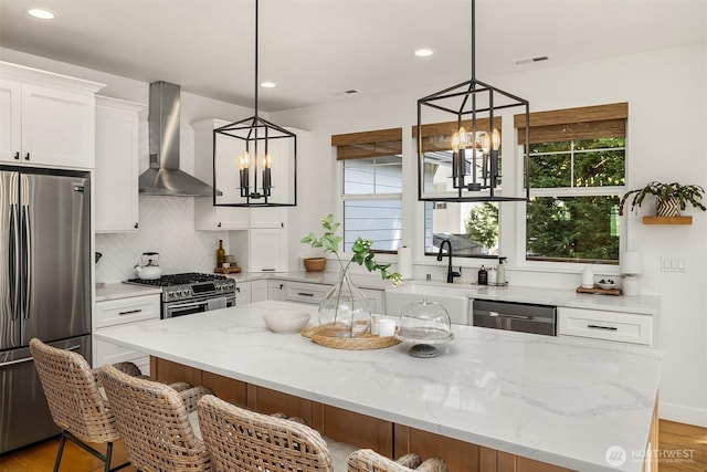 kitchen with stainless steel appliances, wall chimney range hood, a chandelier, decorative backsplash, and recessed lighting