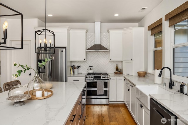 kitchen with stainless steel appliances, wall chimney range hood, a chandelier, backsplash, and white cabinetry