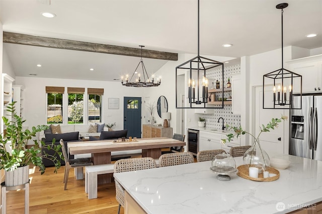 dining area featuring a chandelier, beverage cooler, beam ceiling, light wood-type flooring, and recessed lighting