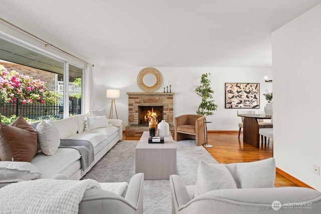 living room with baseboards, a stone fireplace, and wood finished floors