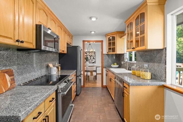 kitchen with glass insert cabinets, stone finish flooring, a sink, decorative backsplash, and appliances with stainless steel finishes