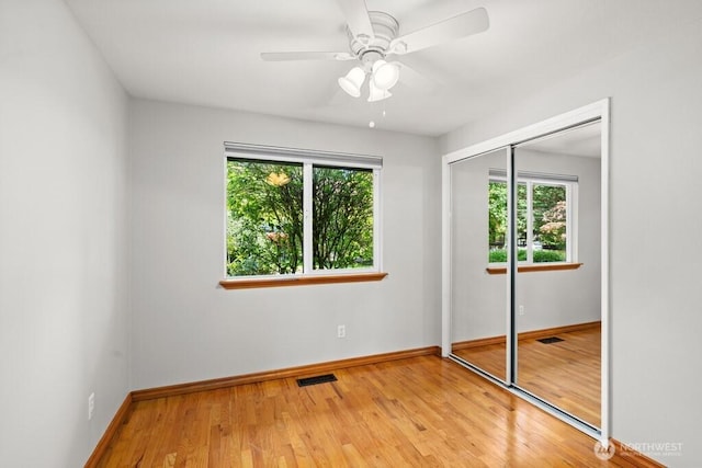 unfurnished bedroom featuring baseboards, a closet, visible vents, and wood finished floors
