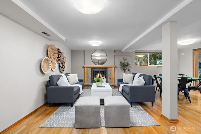 living room with visible vents, wood finished floors, baseboards, and a lit fireplace