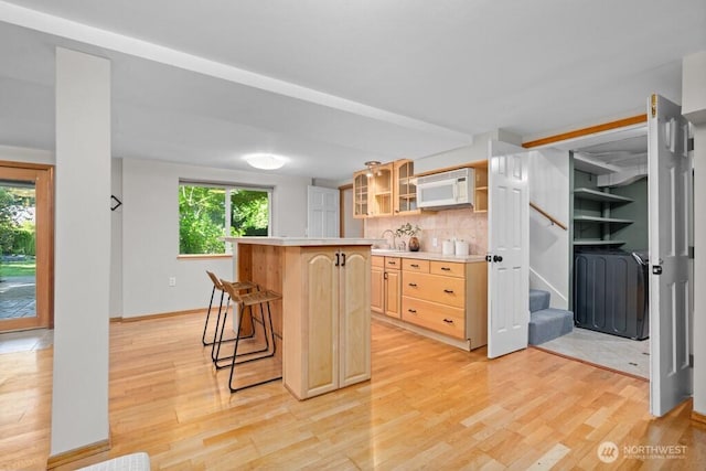 kitchen with light brown cabinets, a breakfast bar area, light wood finished floors, white microwave, and light countertops