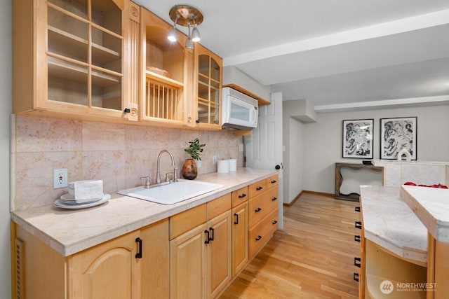 kitchen featuring light wood finished floors, light countertops, white microwave, and a sink