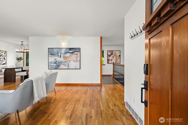 entrance foyer with light wood finished floors, baseboards, visible vents, and a chandelier
