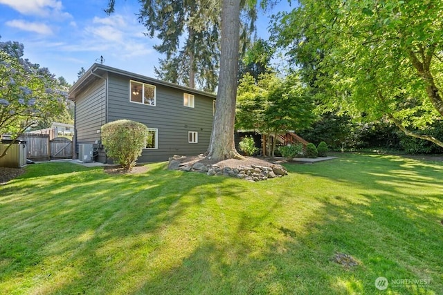 back of property with central air condition unit, a gate, fence, and a lawn