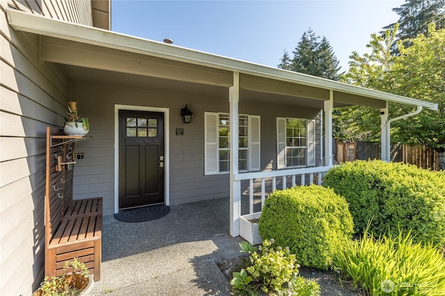 view of exterior entry featuring covered porch and fence