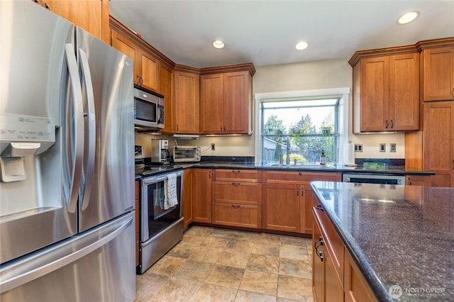 kitchen featuring stainless steel appliances, brown cabinets, recessed lighting, stone finish floors, and dark stone countertops