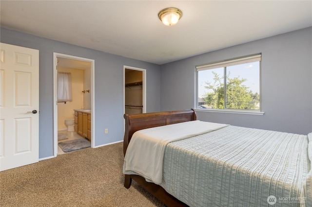 carpeted bedroom with connected bathroom, baseboards, a walk in closet, and a closet