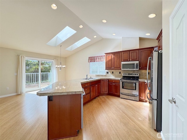 kitchen with appliances with stainless steel finishes, a skylight, a peninsula, a chandelier, and light wood-style flooring