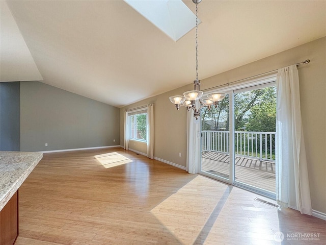 unfurnished dining area featuring a chandelier, lofted ceiling, light wood-style floors, baseboards, and a skylight