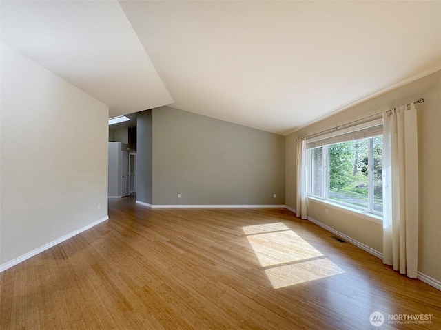 empty room with light wood finished floors, baseboards, and lofted ceiling