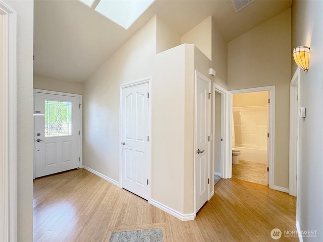entryway featuring high vaulted ceiling, light wood finished floors, baseboards, and a skylight
