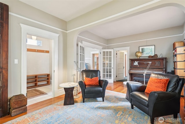 living area with arched walkways, french doors, and light wood-style flooring