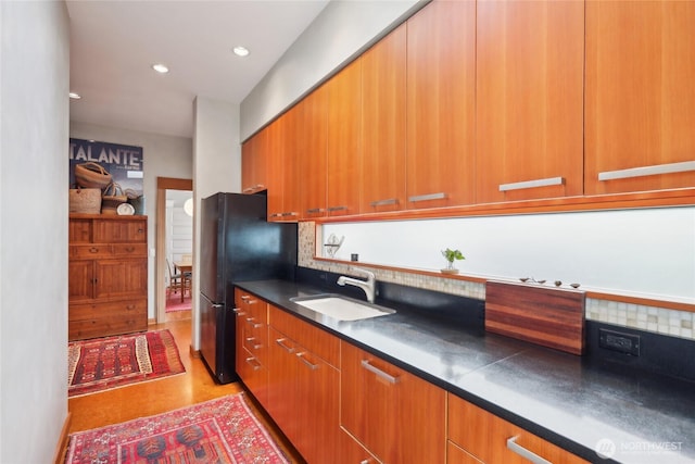 kitchen featuring a sink, freestanding refrigerator, dark countertops, brown cabinetry, and modern cabinets