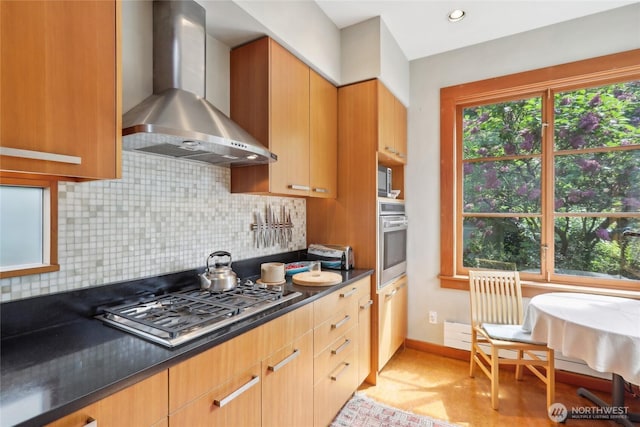 kitchen with stainless steel appliances, wall chimney exhaust hood, tasteful backsplash, and baseboards