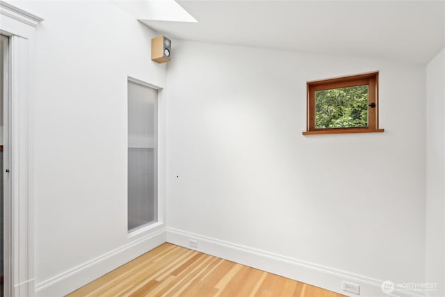 spare room with light wood finished floors, vaulted ceiling, and baseboards
