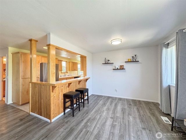 kitchen featuring freestanding refrigerator, wood finished floors, a kitchen breakfast bar, light countertops, and a peninsula