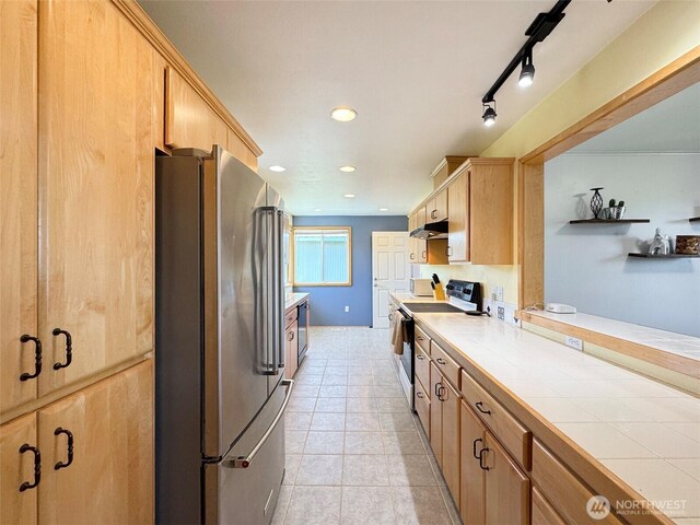 kitchen featuring freestanding refrigerator, electric range, under cabinet range hood, tile countertops, and light brown cabinetry