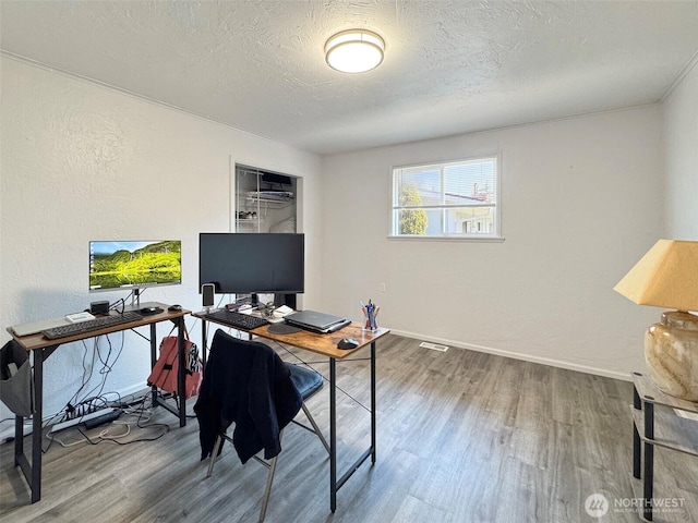 office area with wood finished floors, a textured ceiling, baseboards, and a textured wall