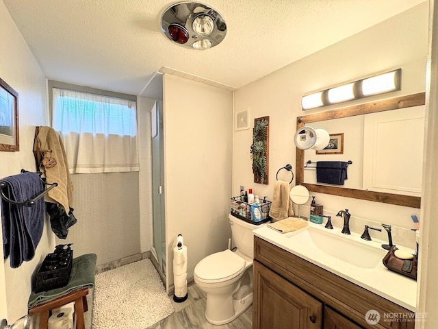 bathroom featuring a stall shower, a textured ceiling, toilet, and vanity
