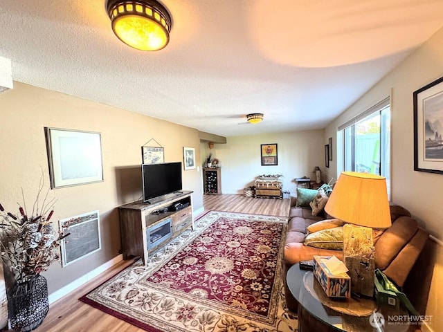 living area with wood finished floors, baseboards, a textured ceiling, and heating unit