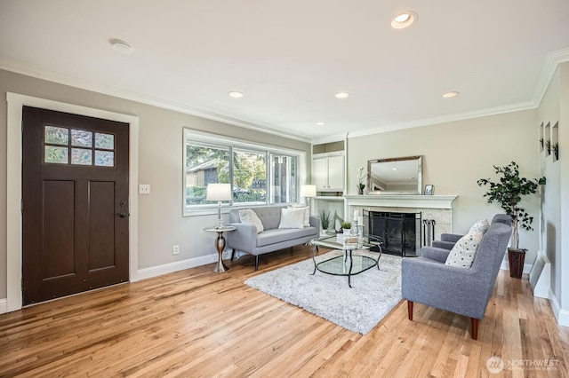 living area with baseboards, ornamental molding, light wood-style floors, a fireplace, and recessed lighting