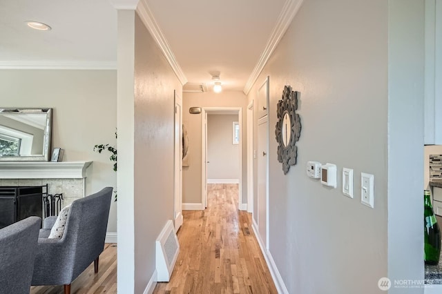 hallway with light wood-style flooring, crown molding, and baseboards