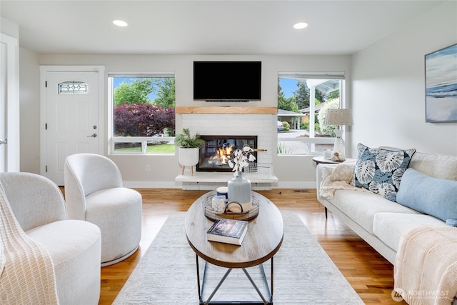 living room with a brick fireplace, healthy amount of natural light, recessed lighting, wood finished floors, and baseboards