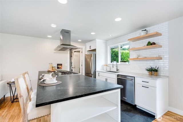 kitchen featuring appliances with stainless steel finishes, open shelves, island range hood, a sink, and white cabinets