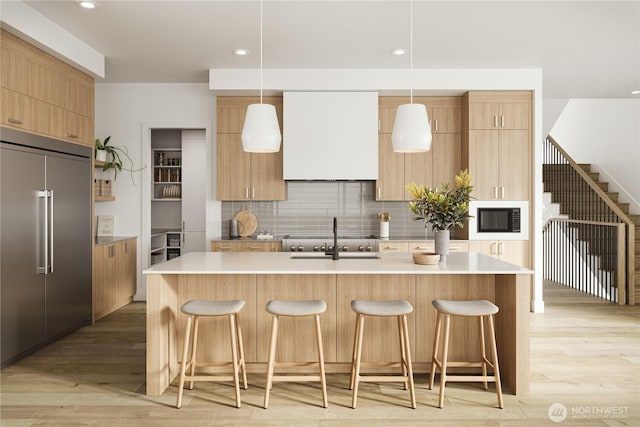 kitchen featuring built in appliances, a kitchen bar, a sink, light wood-type flooring, and recessed lighting