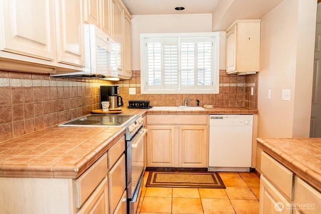 kitchen featuring white appliances, tile counters, tasteful backsplash, light tile patterned floors, and a sink