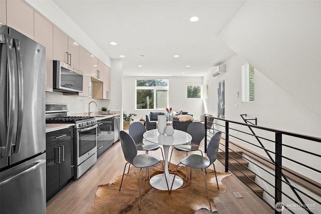 kitchen with stainless steel appliances, an AC wall unit, a sink, light wood-style flooring, and recessed lighting